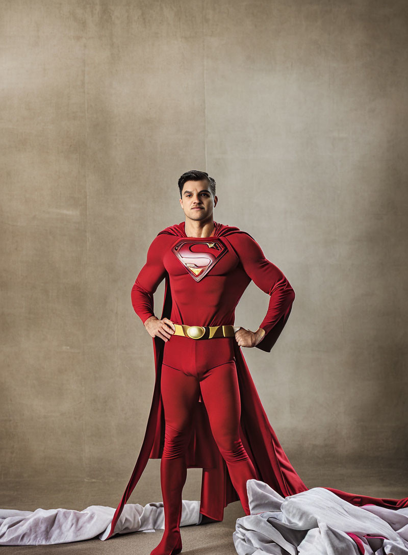 Person in Superman costume posing confidently against beige backdrop