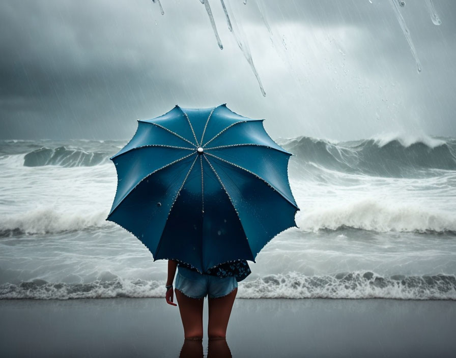 Blue umbrella person faces turbulent ocean waves on rainy day.