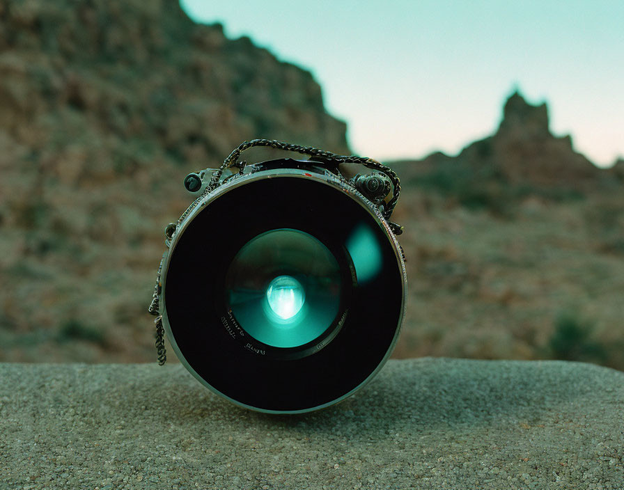 Large Camera Lens on Rock with Desert Mountain Landscape at Twilight