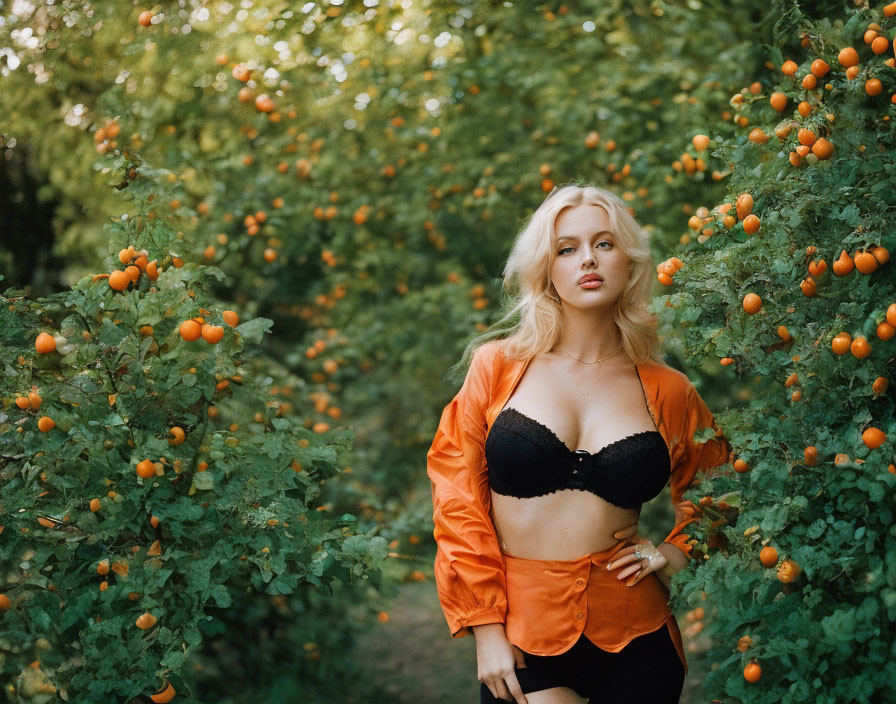 Woman in Black Bra and Orange Jacket Surrounded by Lush Greenery and Orange Fruits