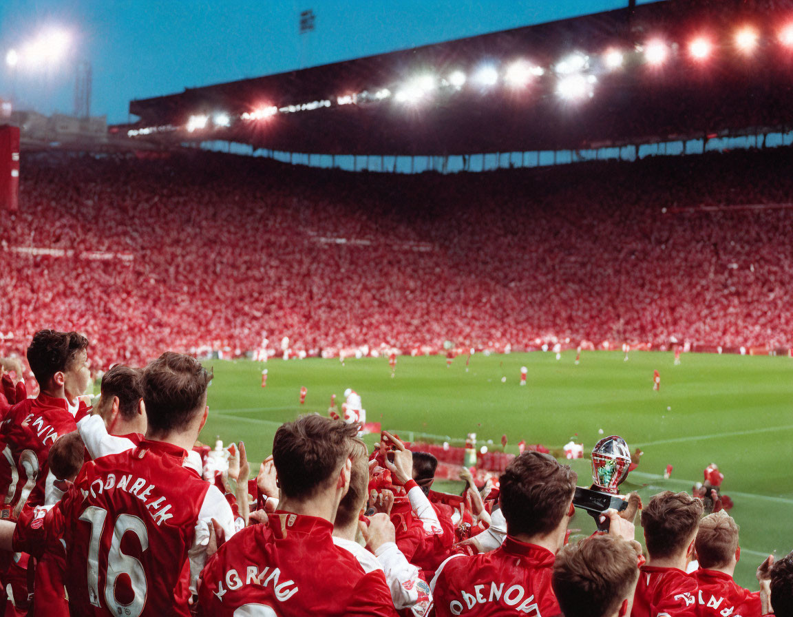 Red-clad crowd at vibrant football stadium with players and trophy.