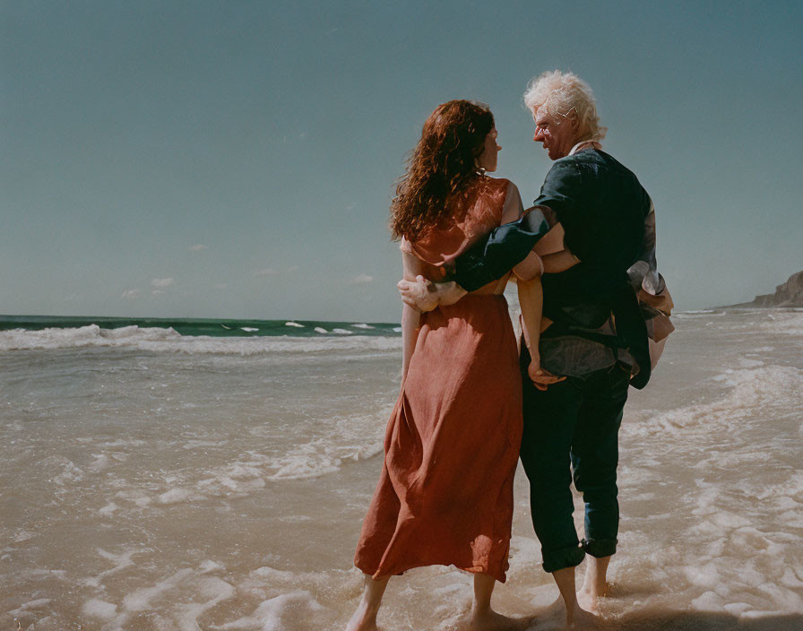 Smiling older man carries happy young girl on sunny beach