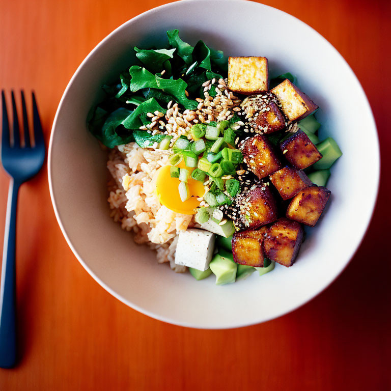 Bowl of rice with fried egg, tofu, vegetables, and sesame seeds