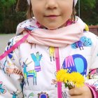 Young girl with blue eyes in white beanie and floral jacket holding yellow flowers