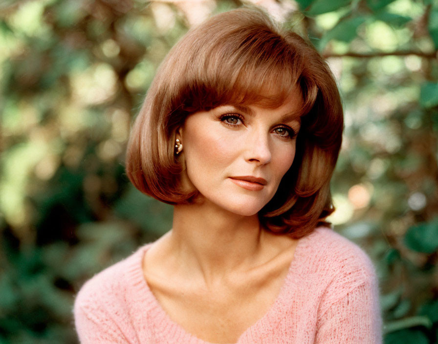 Auburn-haired woman in pink knit top with gold earrings gazes serenely.