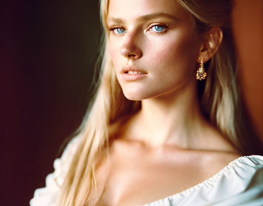 Blonde woman in white dress with blue eyes and floral earring in warm setting