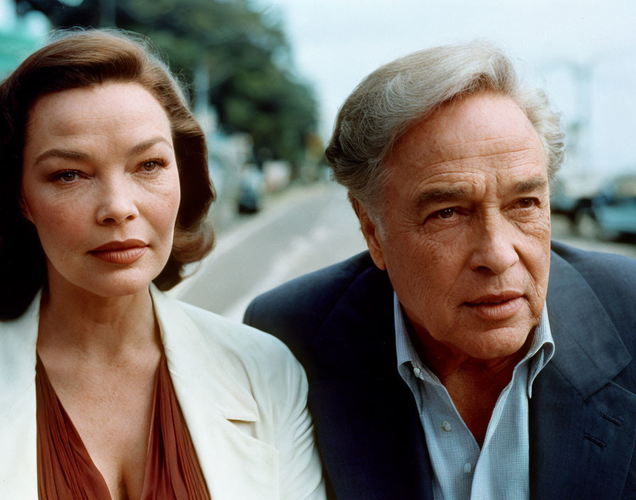 Serious man in suit and woman with scarf in car gaze into distance