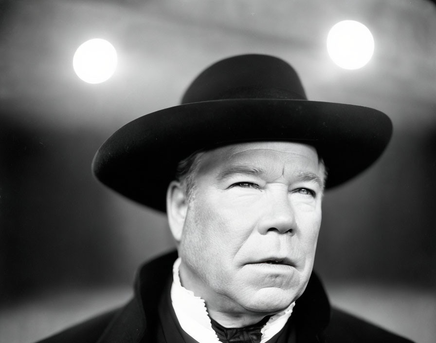 Monochrome image of person in wide-brimmed hat with blurred lights