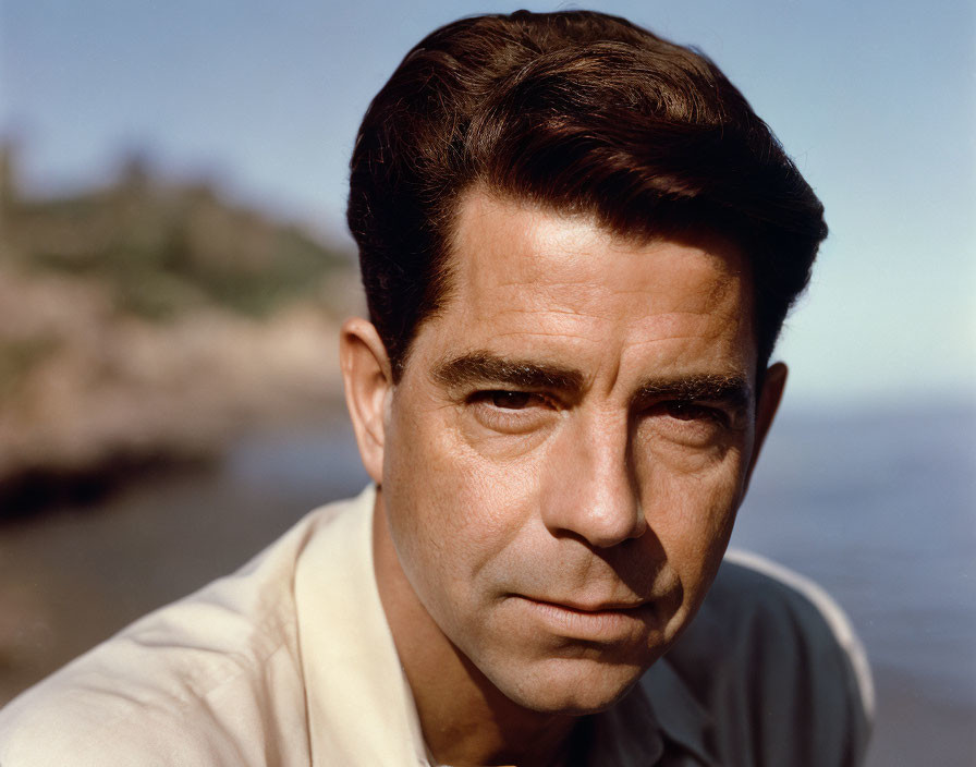 Middle-aged man portrait with dark hair and serious expression in light beige shirt.