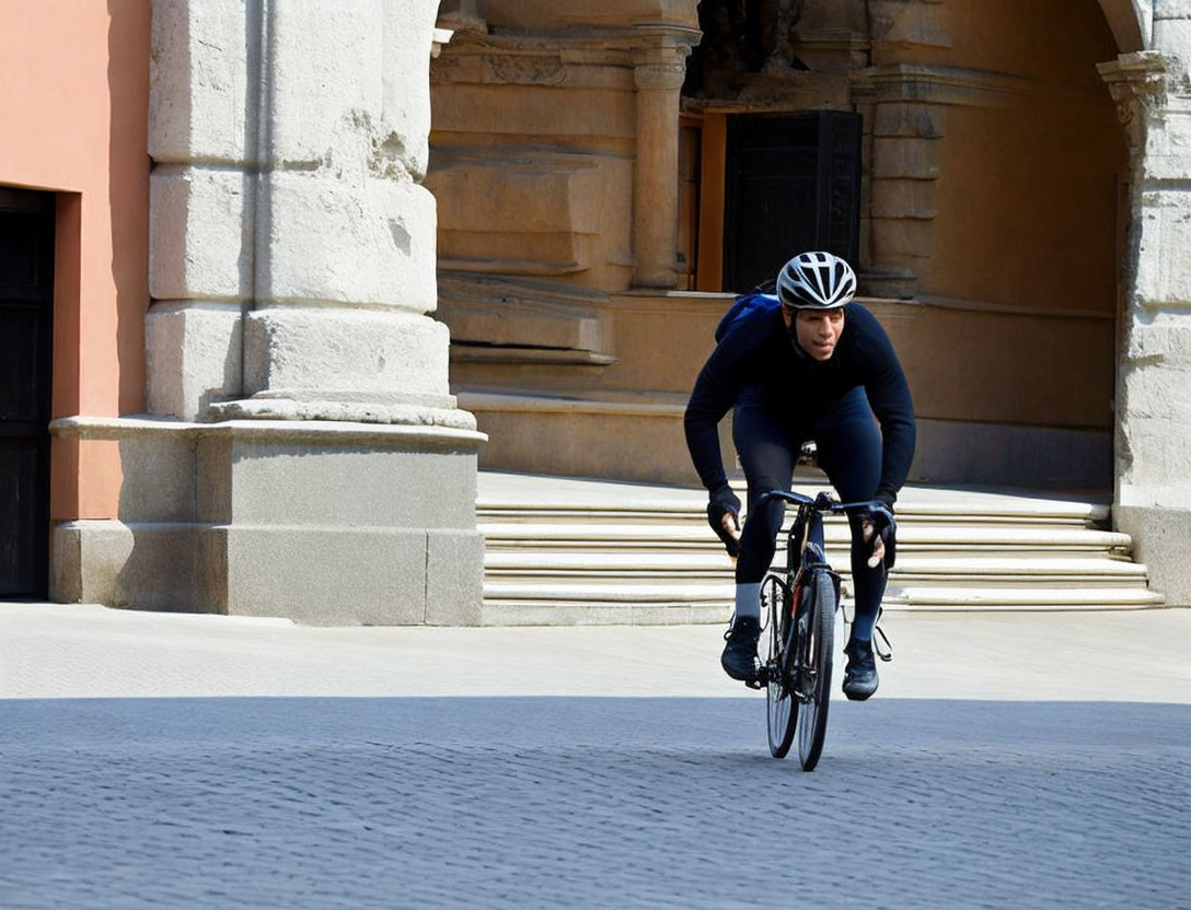 Cyclist in black attire rides past classical building and columns