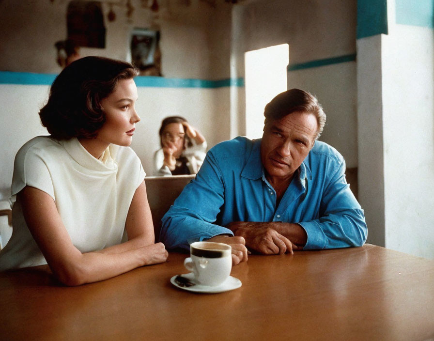 Man in blue shirt and woman in white top share coffee at café table