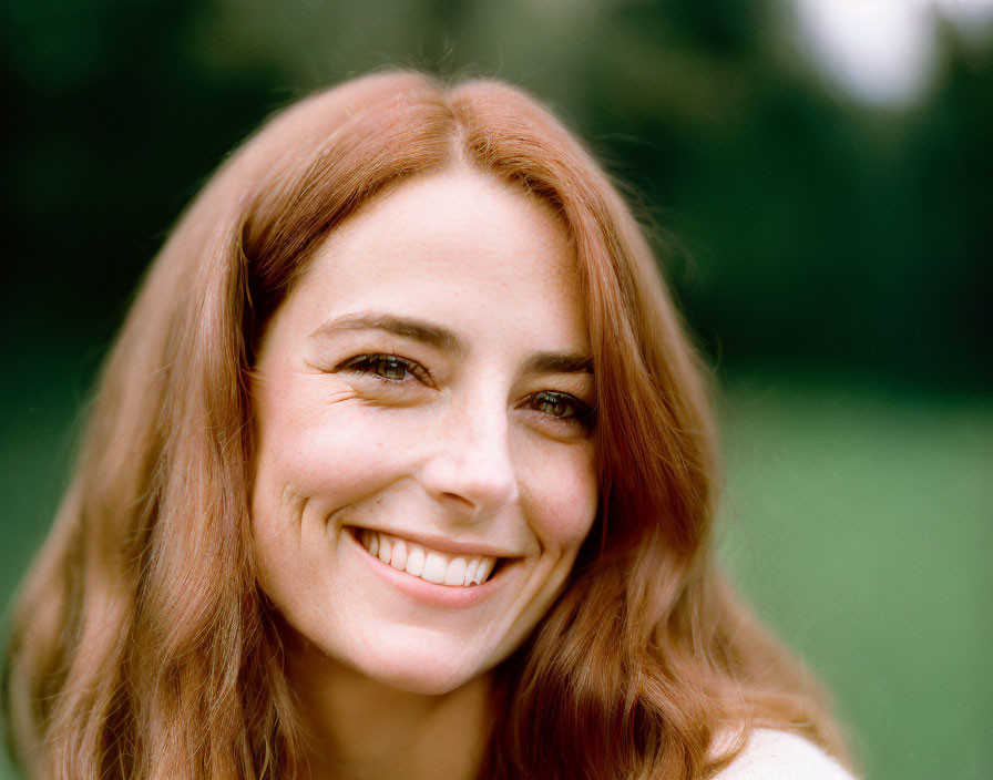 Red-haired woman with green eyes smiling against blurred green backdrop