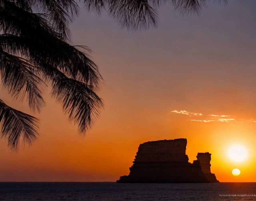 Tranquil beach sunset with sun near horizon and rock formation