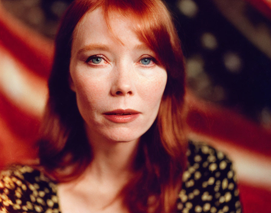 Red-haired woman in black and gold top poses with American flag