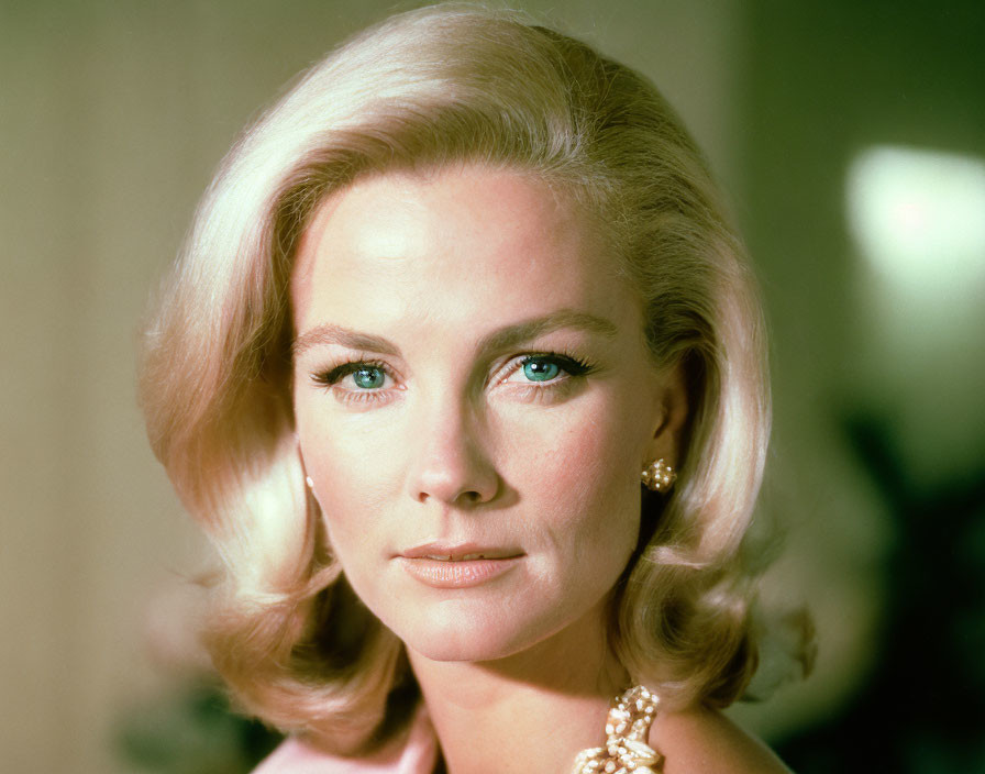 Blonde woman with green eyes wearing pearl jewelry gazes at camera