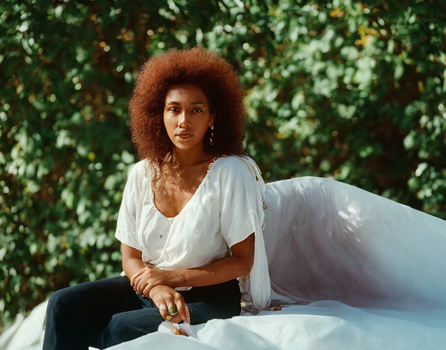 Woman with Afro Hairstyle Sitting Outdoors Surrounded by Green Foliage