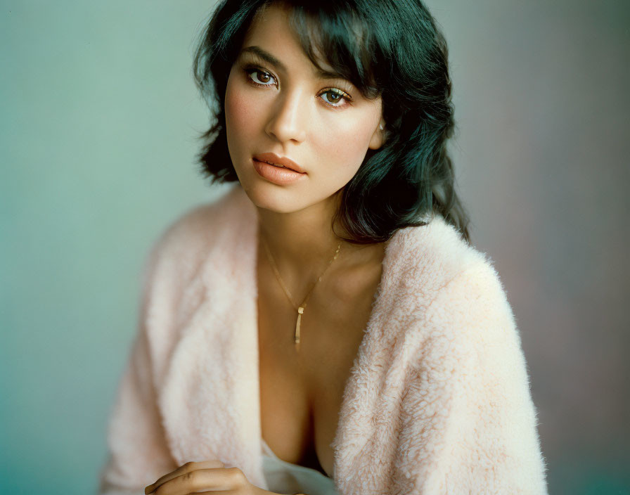 Woman with short dark hair in light pink fuzzy garment on soft blue background