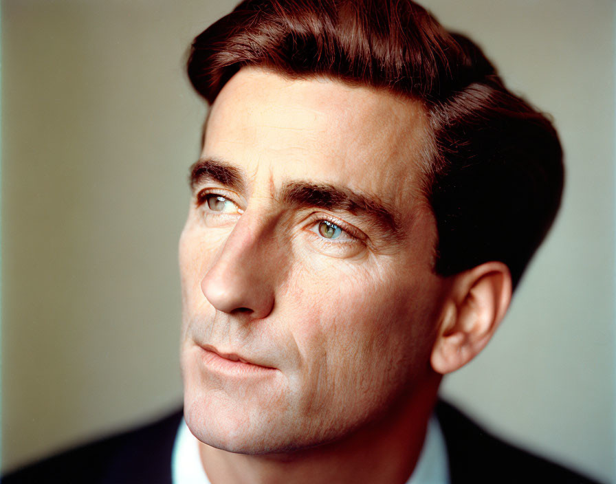 Portrait of man with dark hair, prominent eyebrows, and blue eyes on neutral background