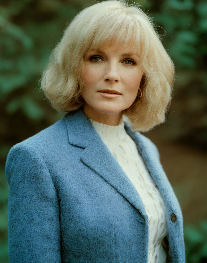 Blonde woman in blue coat and white sweater on green background