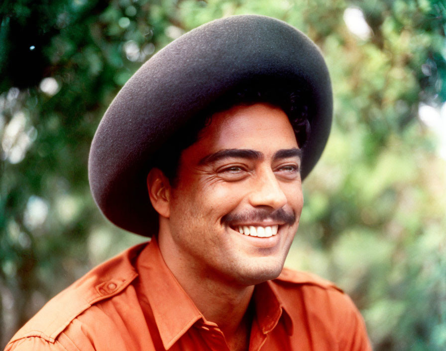 Smiling person in broad-brimmed hat and orange shirt on green background