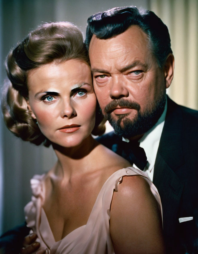 Vintage portrait of a woman and man in formal attire with curled hair and a beard.