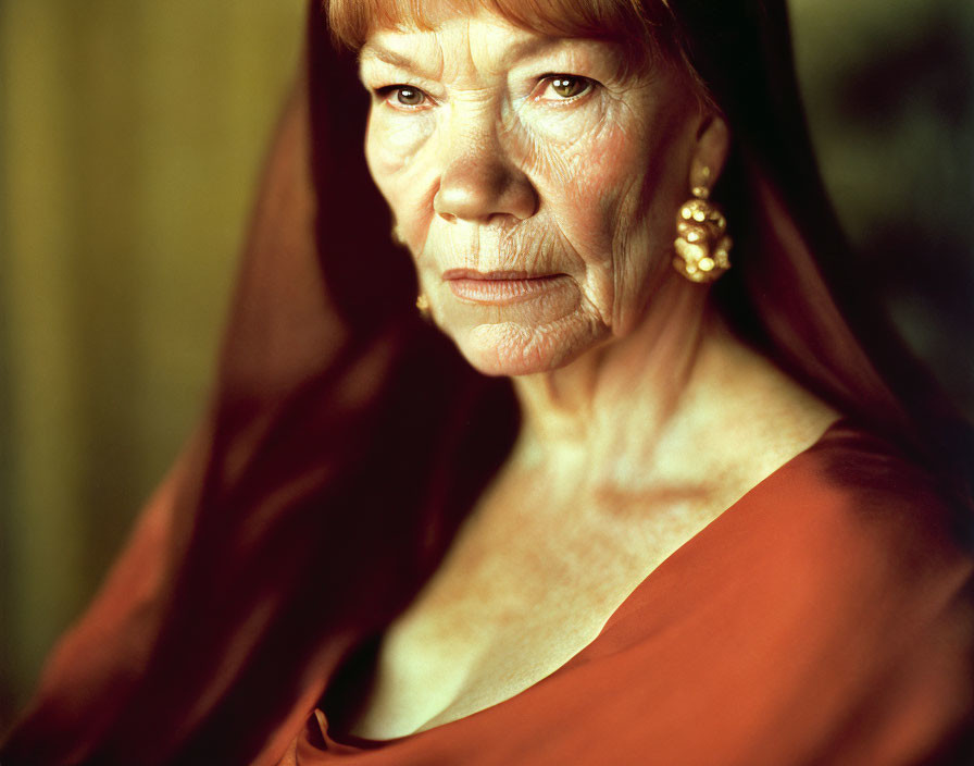 Elderly woman in red attire and earrings gazes at camera