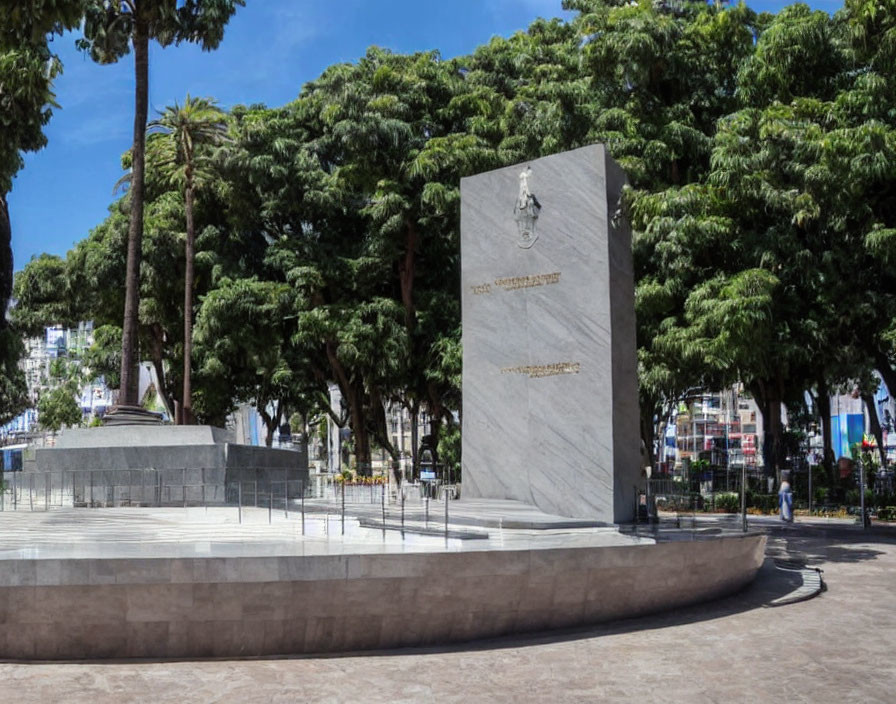 Monument with inscriptions in lush green plaza surrounded by palm trees