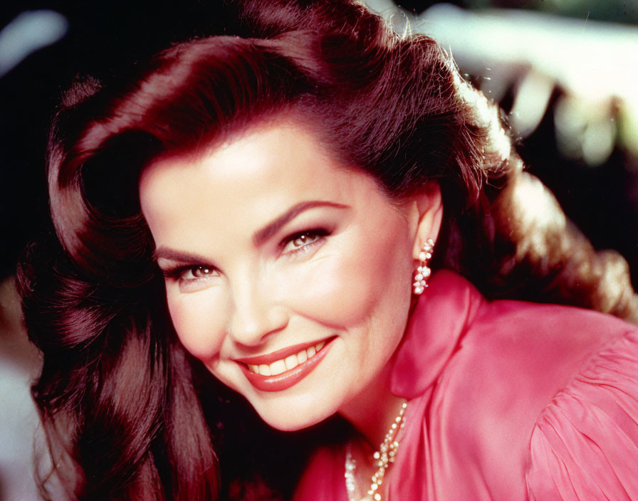 Smiling woman with dark hair in red attire and diamond earrings