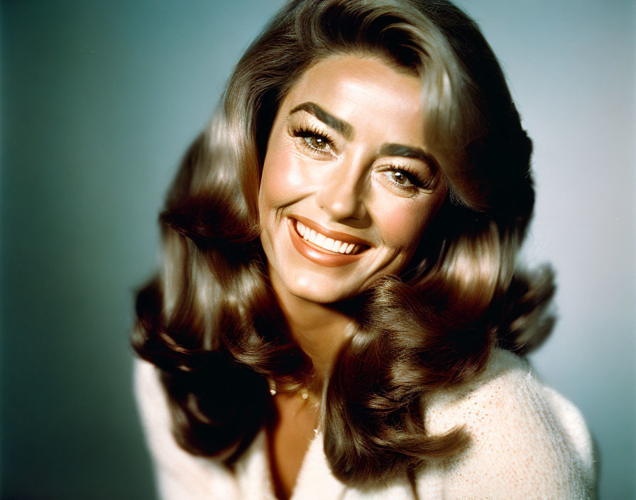 Smiling woman with voluminous brown hair and striking eye makeup in white outfit