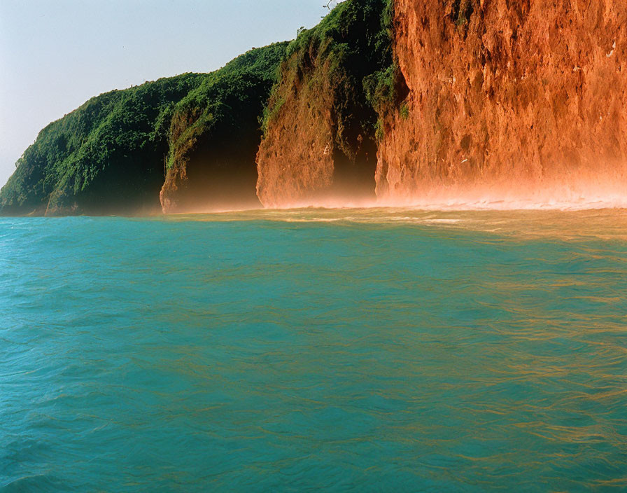 Cliff with lush greenery and turquoise waters under misty sunlight