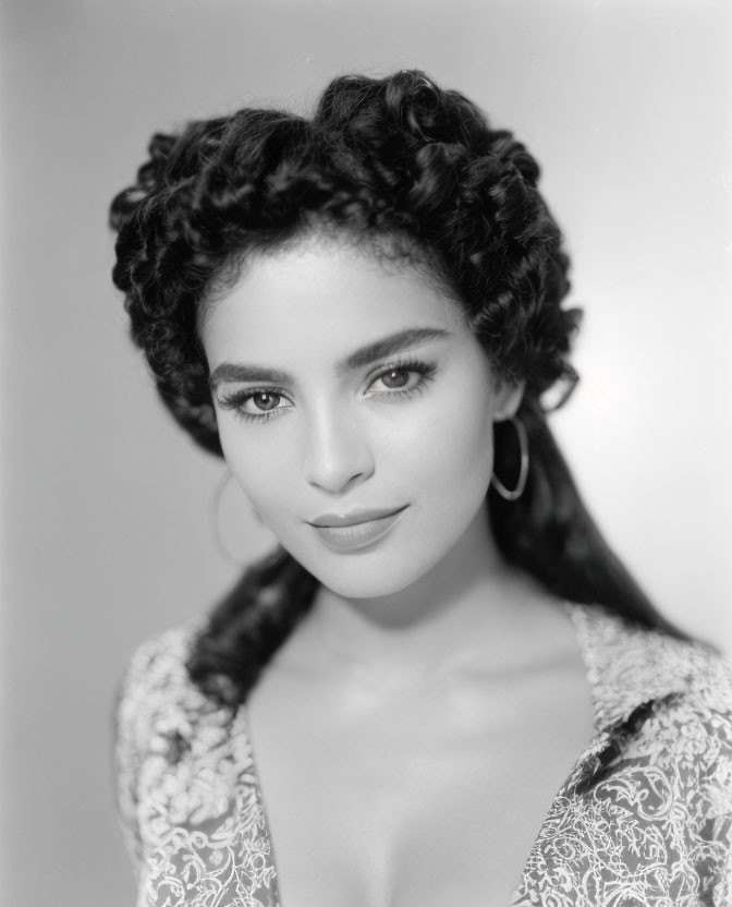 Portrait of a woman with braided hair, hoop earrings, and lace top.