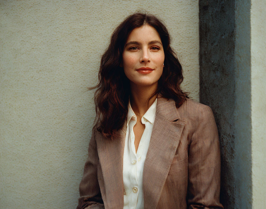 Brunette woman in brown blazer and white shirt smiling in front of textured wall