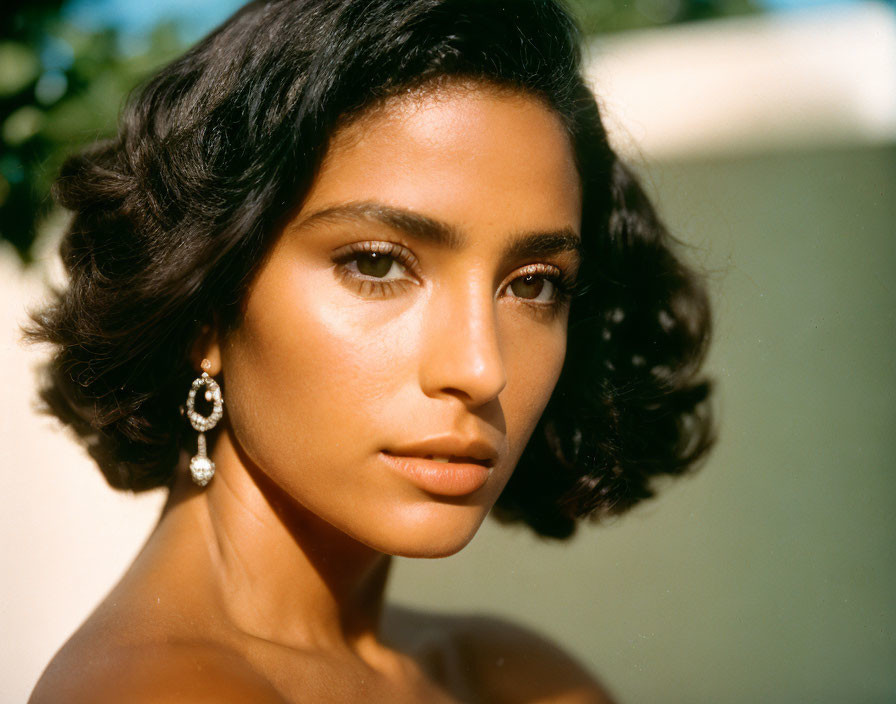 Portrait of woman with short wavy hair and elegant earrings in soft sunlight.