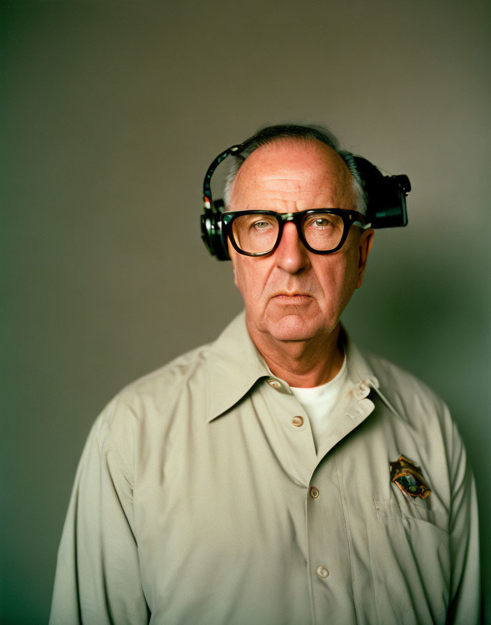 Elderly man in glasses with headset and badge, serious expression