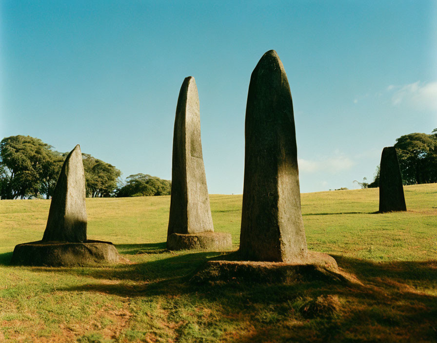 Four Pointed Stone Monoliths in Grass Field with Trees and Blue Sky