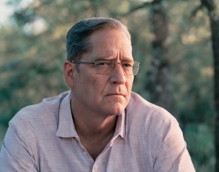 Elderly man in pink checkered shirt gazes into the distance.