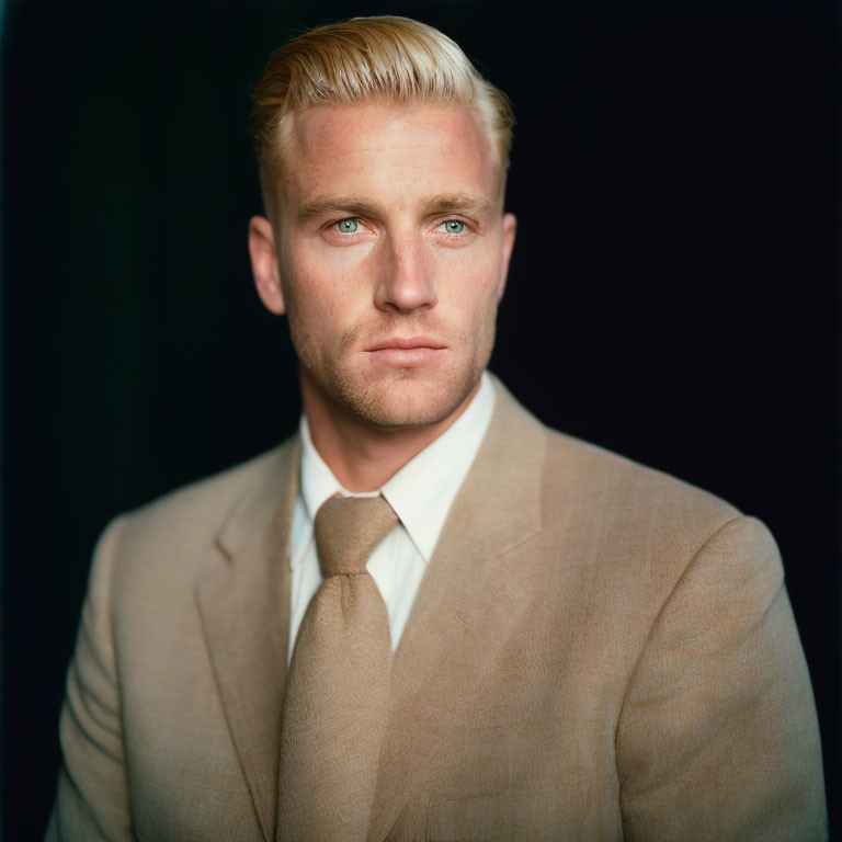 Blond Man in Tan Suit Against Dark Background