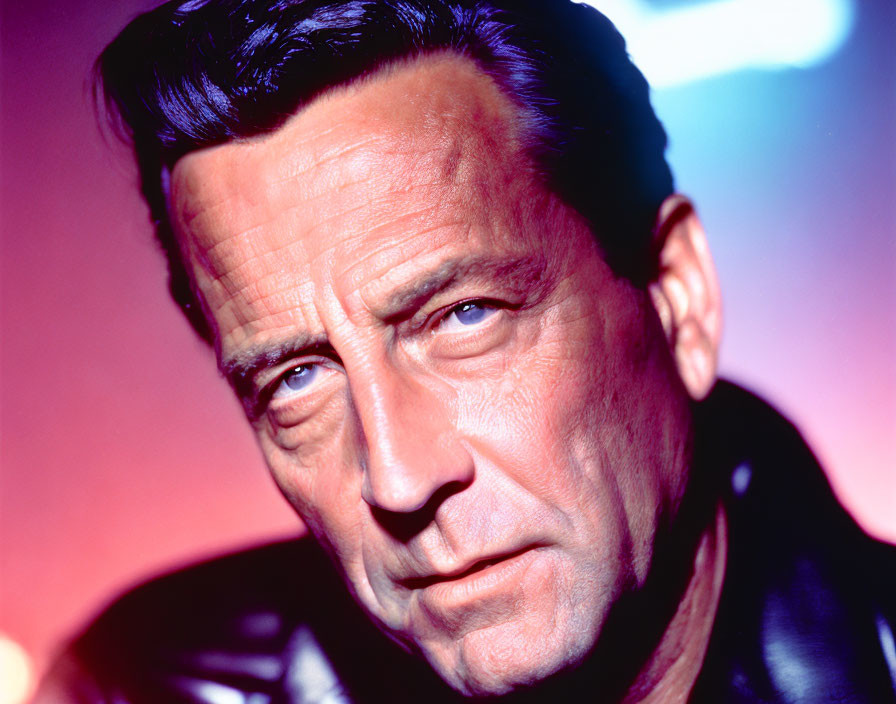 Stern man in black leather jacket on reddish-pink backdrop