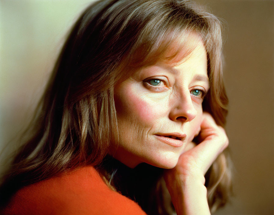 Woman in orange top with hand on cheek, smiling subtly.