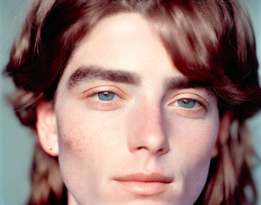 Portrait of person with blue eyes, wavy hair, and freckles gazing at camera