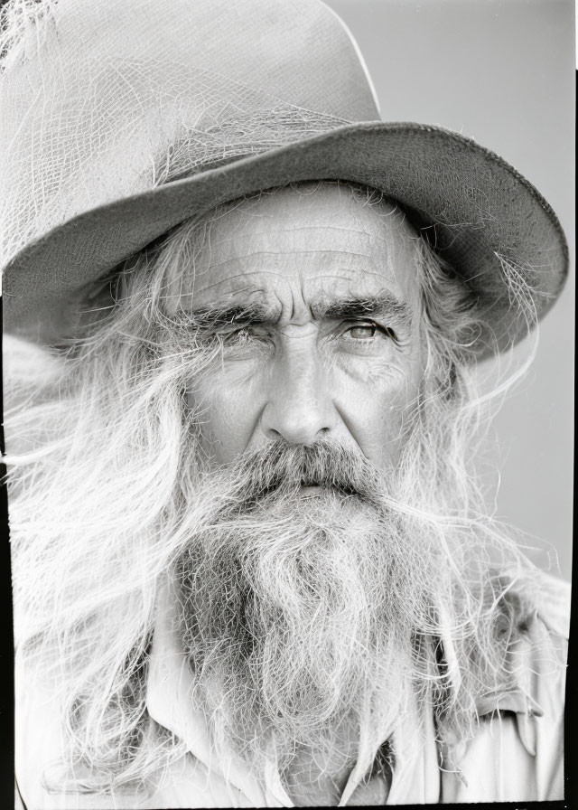 Elderly man with long white beard and hat gazes at camera