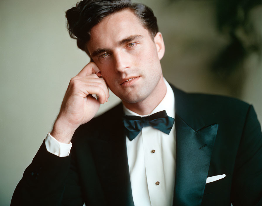 Dark-haired man in black tuxedo and bow tie posing thoughtfully