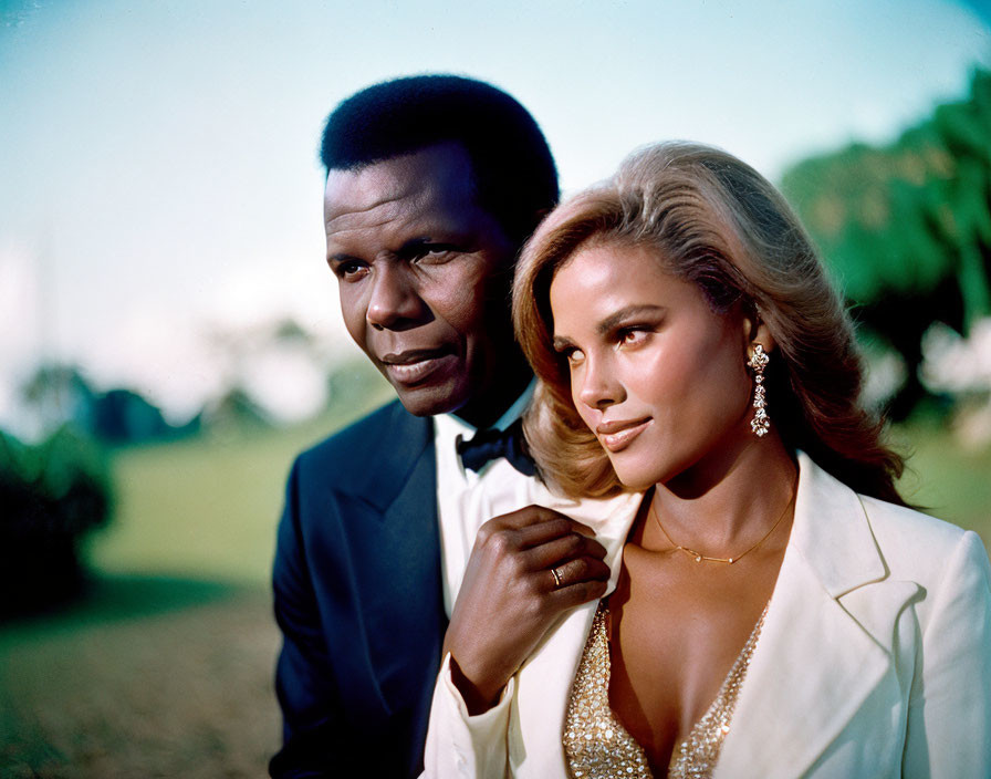 Formal couple in tuxedo and white outfit with necklace posing together