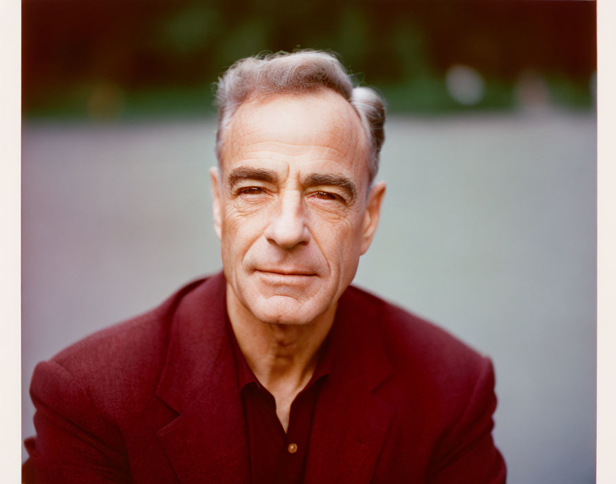 Gray-haired man in maroon shirt gazes at camera