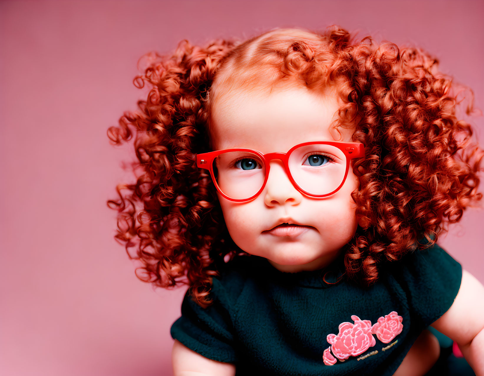 Toddler with red curly hair and glasses on pink background