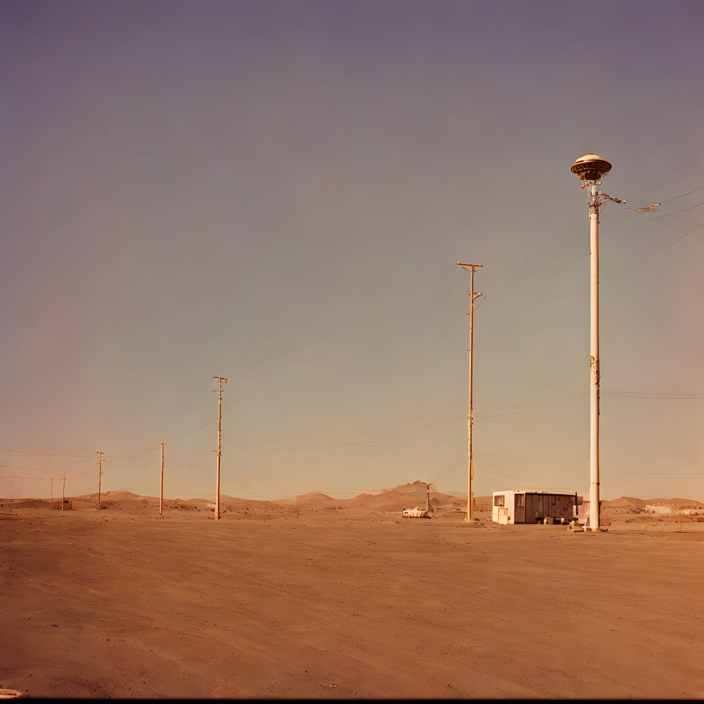 Desert landscape with telephone poles and a solitary building at dusk