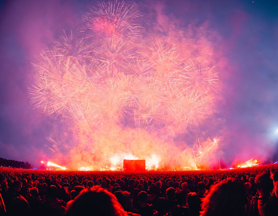 Colorful firework display lights up night sky above outdoor event crowd