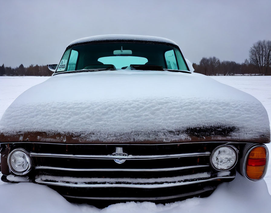 Vintage car in snow-covered field with unique grille and round headlights