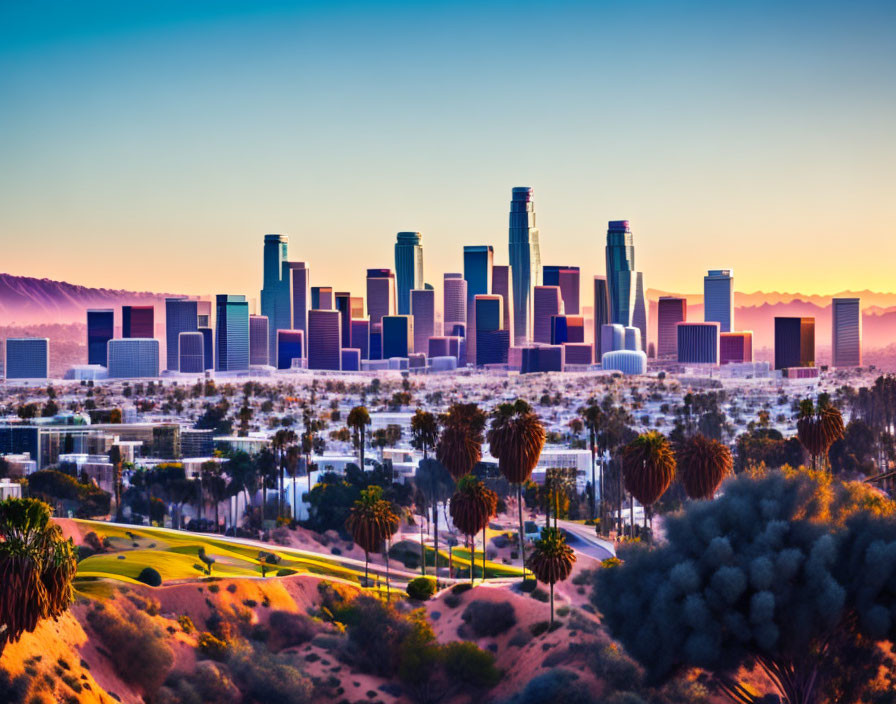 Colorful Los Angeles skyline sunset with palm trees and mountains.