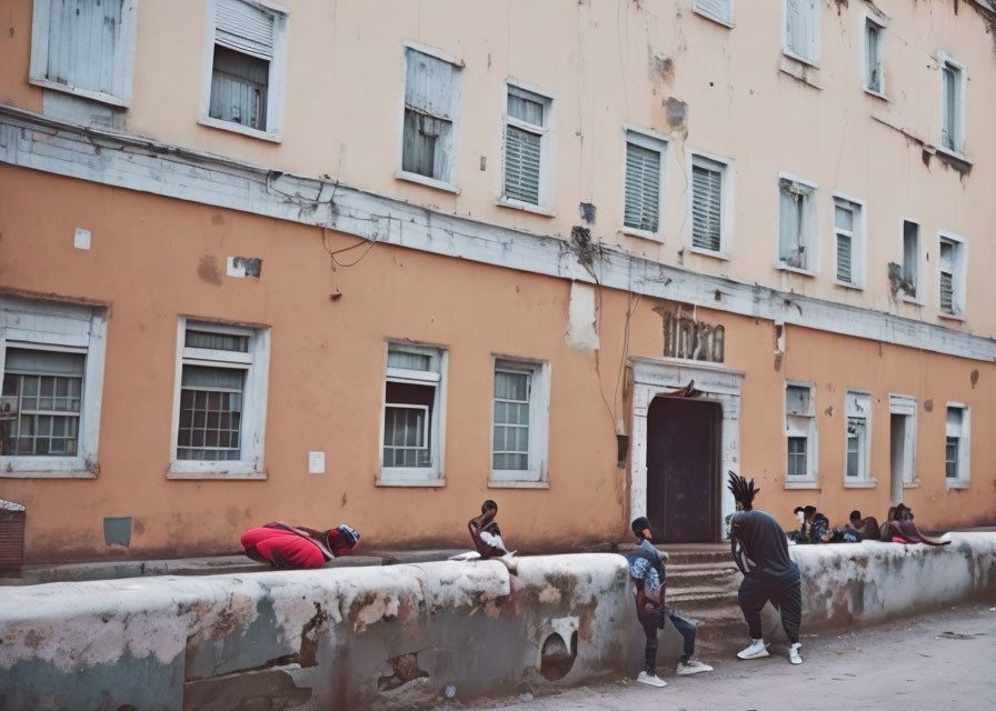 Group of people engaging in activities outside worn-down peach-colored building